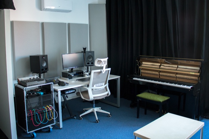 Vista general de la sala de control con monitores, mesa y piano al fondo